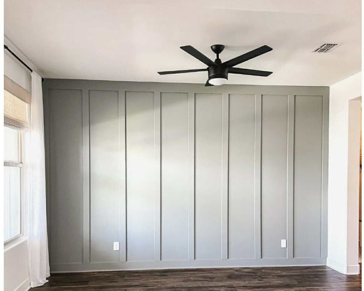 Room with gray vertical paneled wall, dark wood floor, white ceiling, and black ceiling fan.