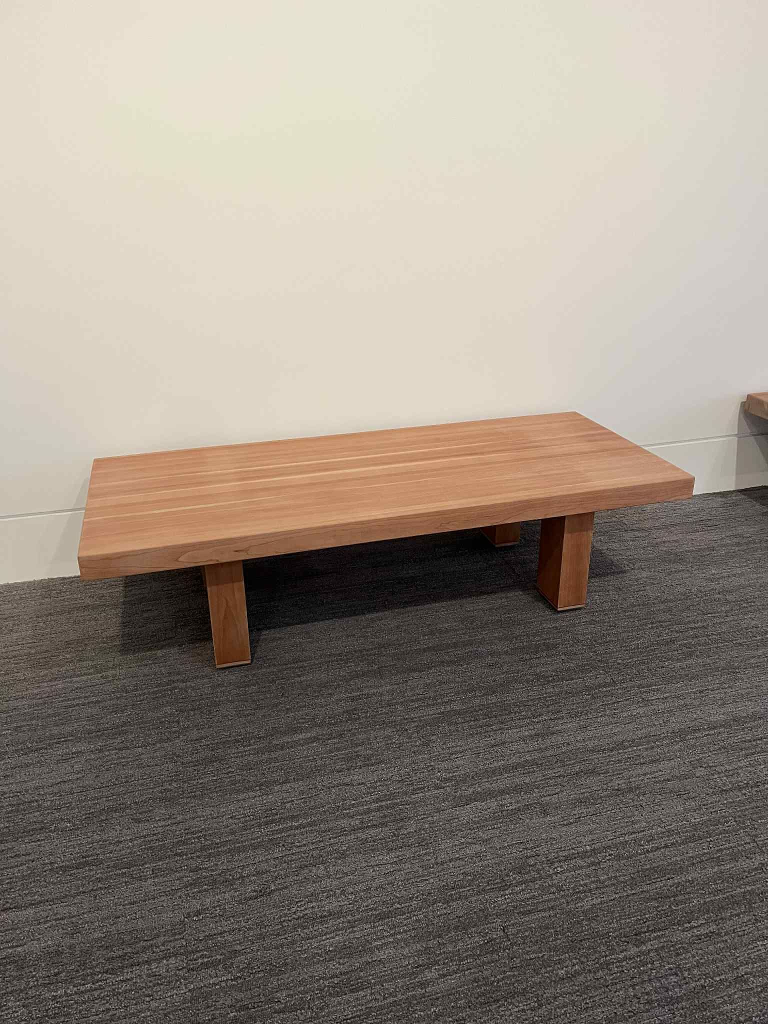 Low wooden bench against a white wall on a gray carpet.