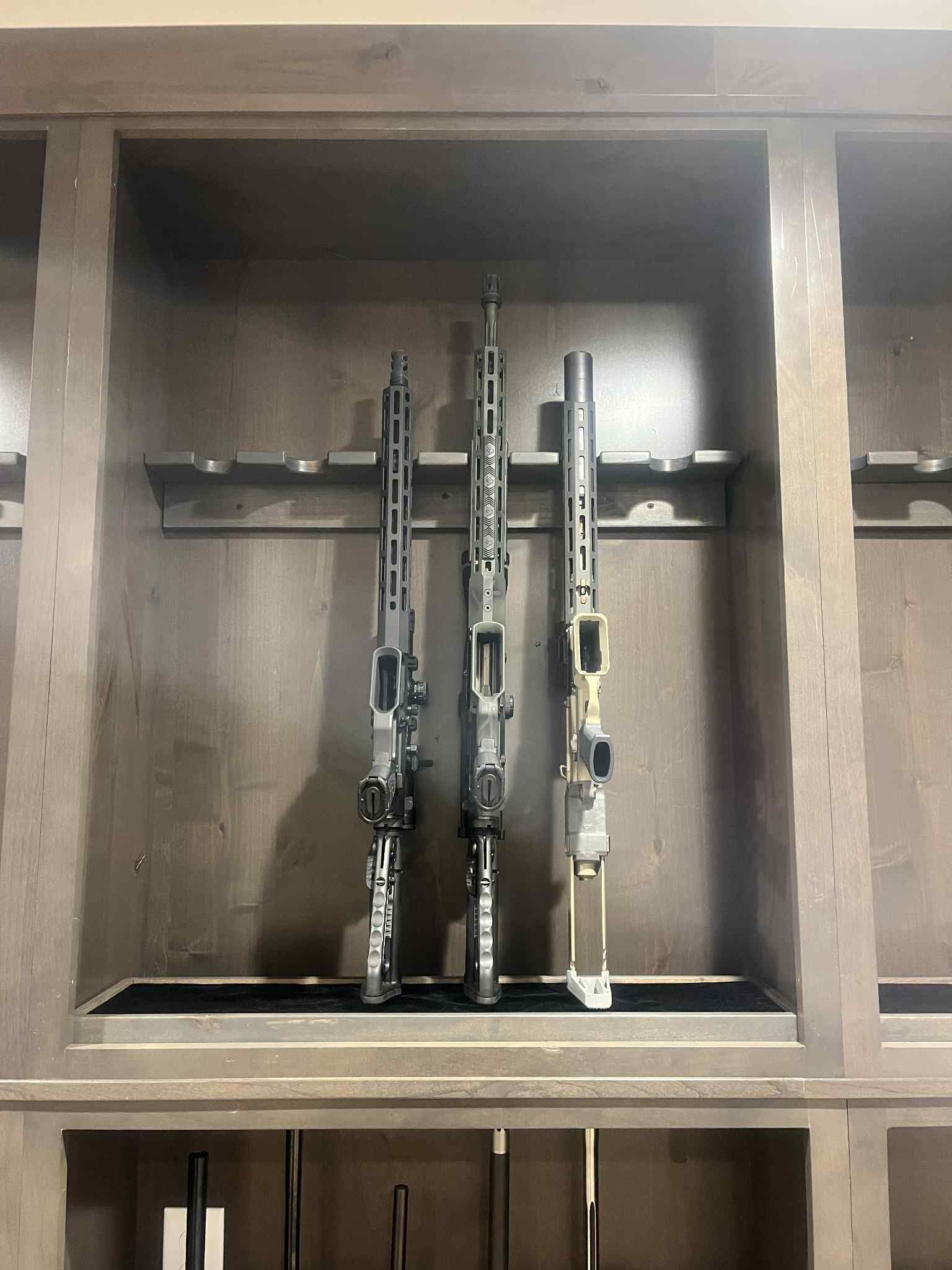 Three rifles displayed upright in a wooden gun cabinet.