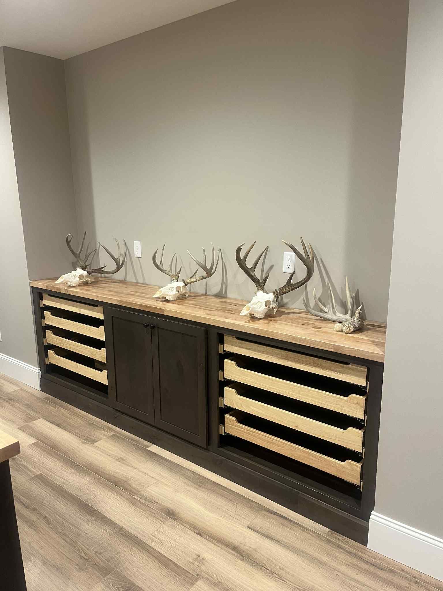 A display cabinet with deer skulls and antlers on a wooden countertop against a gray wall.