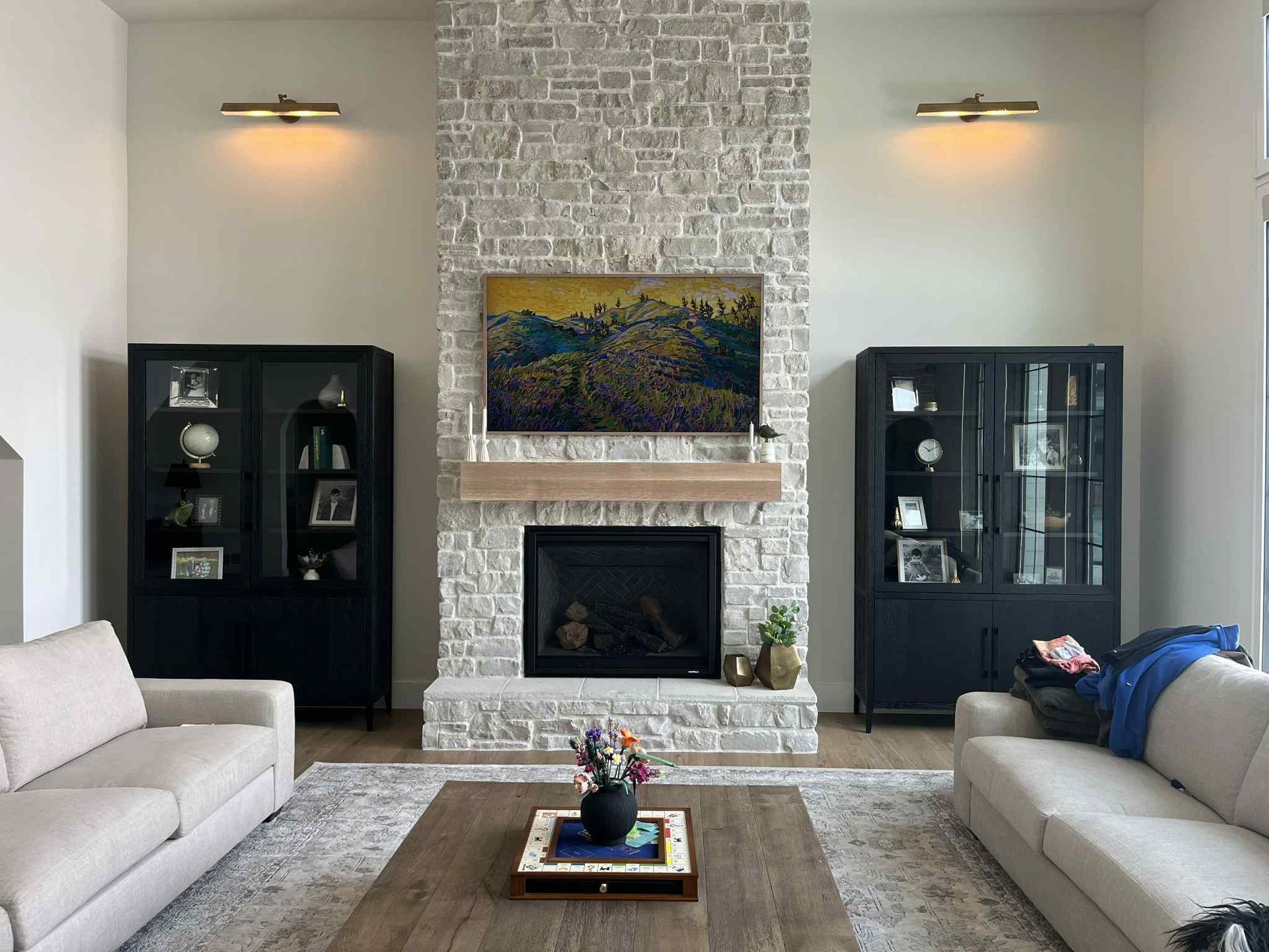 Living room with stone fireplace, flanked by black display cabinets, two sofas, and a coffee table.