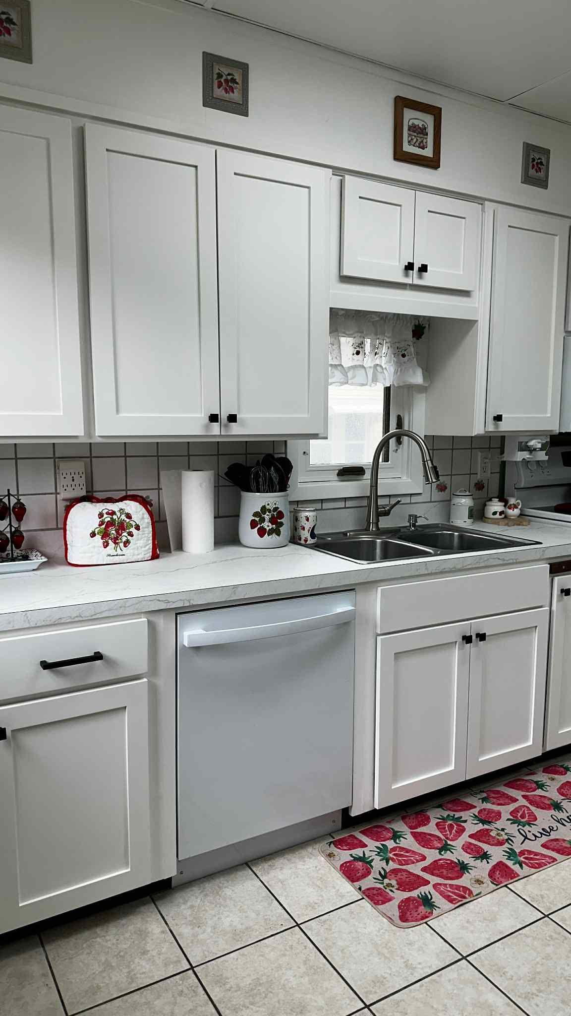 White kitchen with white cabinets, stainless steel appliances, and floral rug.