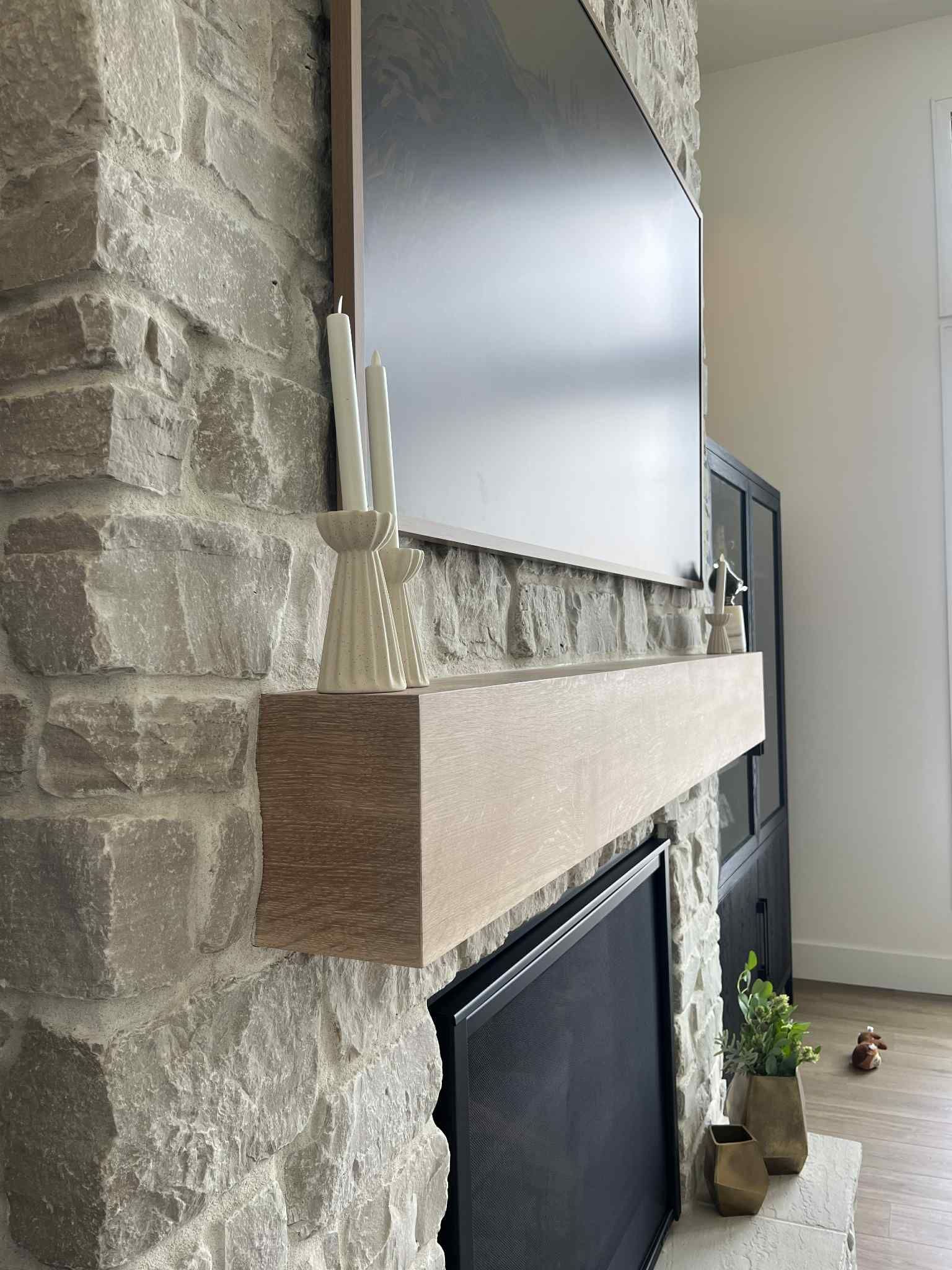 Stone fireplace with wooden mantle holding candles, black TV above.