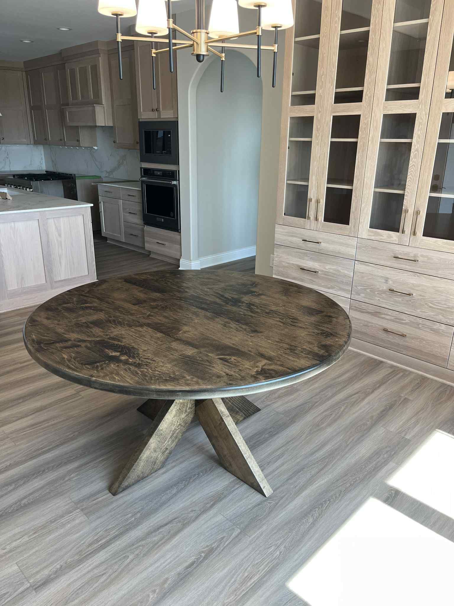 Round dining table with dark textured top and wood starburst base in a modern kitchen.