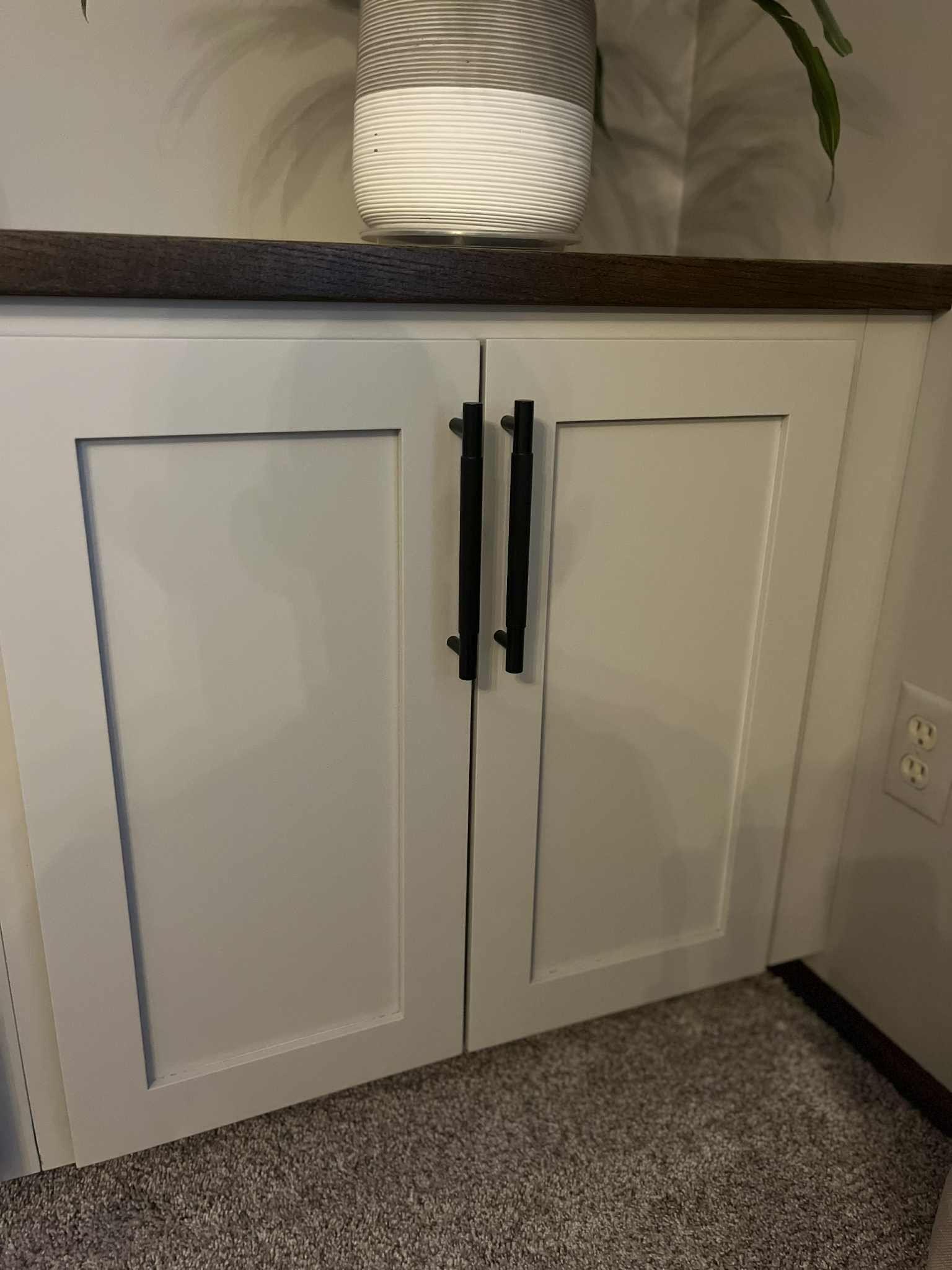 White cabinet doors with black handles, set under a dark wood counter.