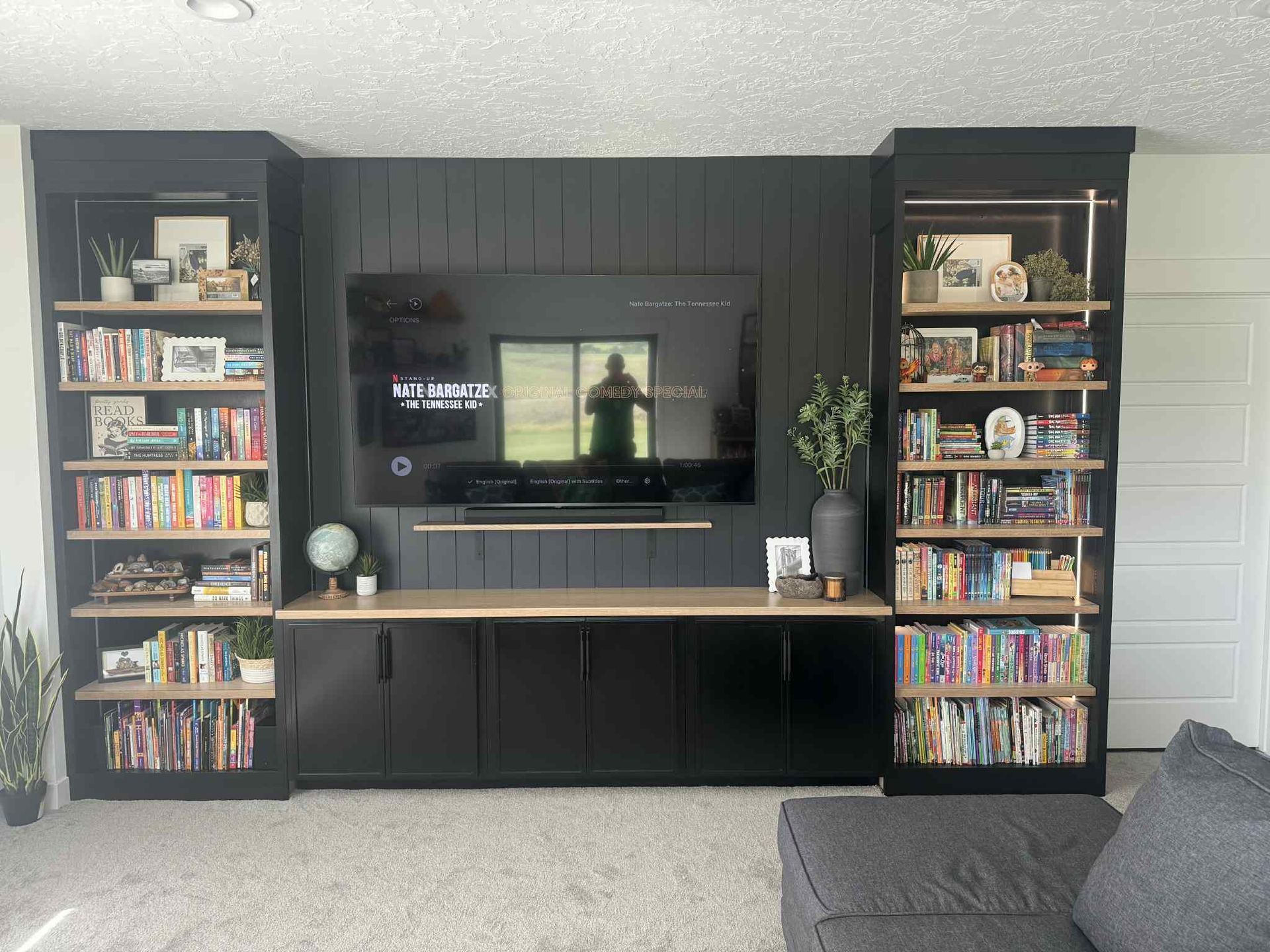 Built-in entertainment center with black cabinetry, a large TV, and open shelving filled with books, plants, and decor.