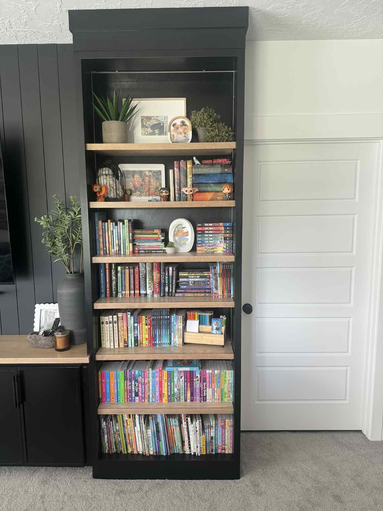 Tall black bookshelf with wood shelves, filled with books, decor, next to a white door.