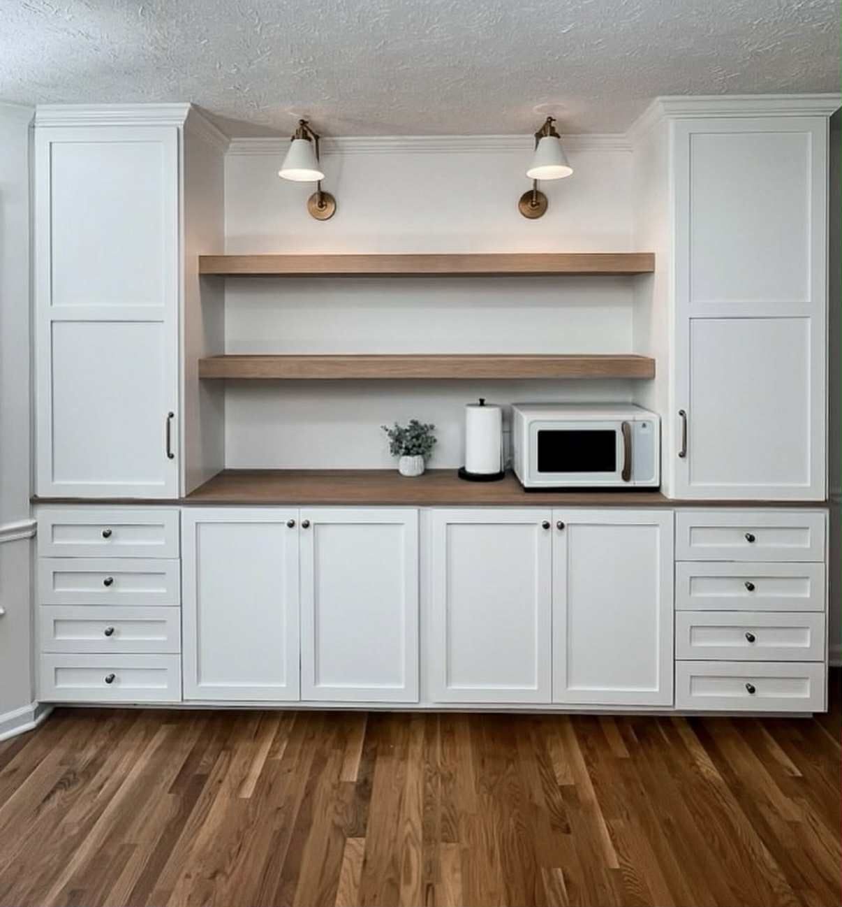 Built-in white cabinets with wood shelves, countertop, and floors. Includes a microwave, paper towel holder, and lights.