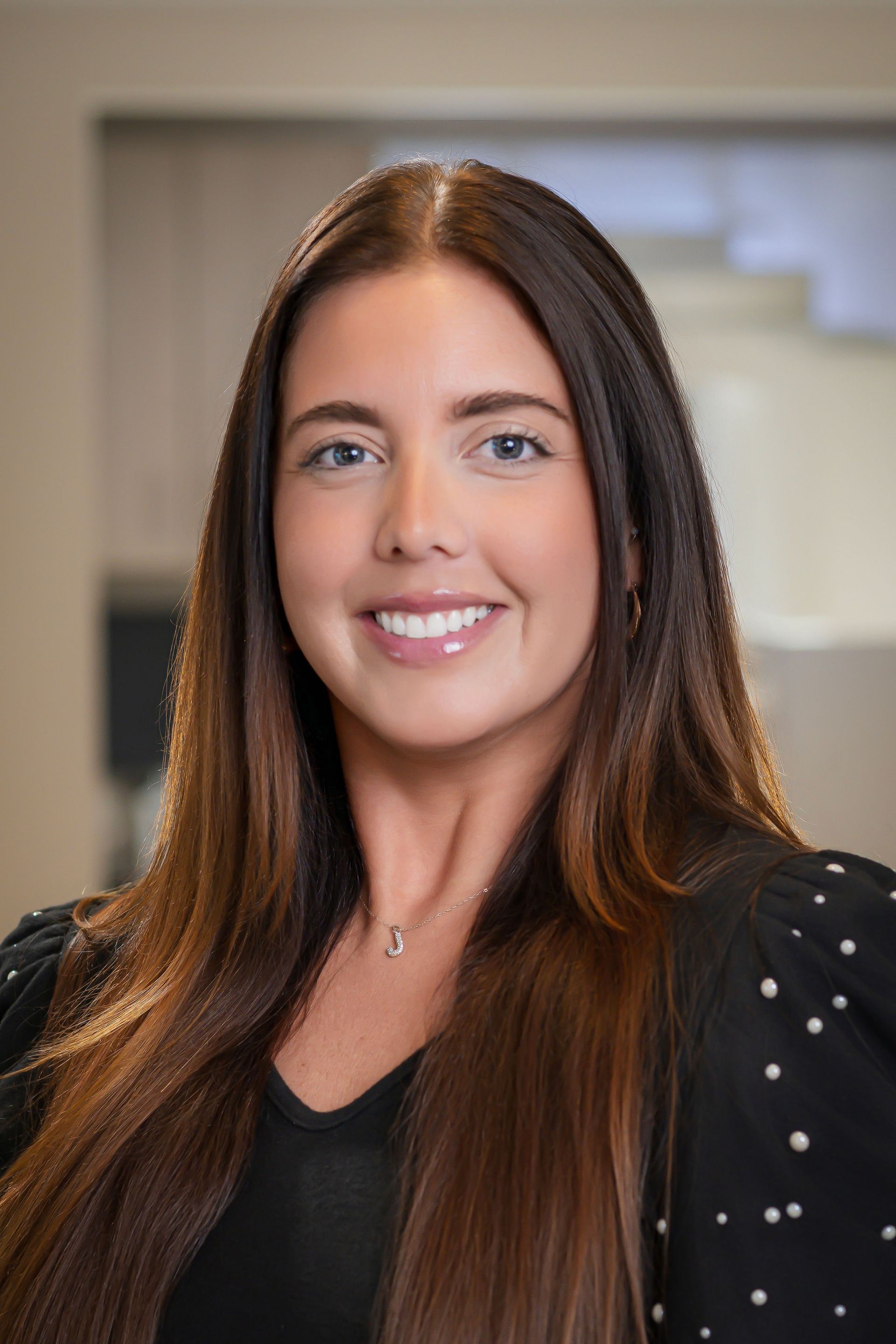 Woman with long brown hair, smiling, in a professional setting, wearing a black top with white dots.