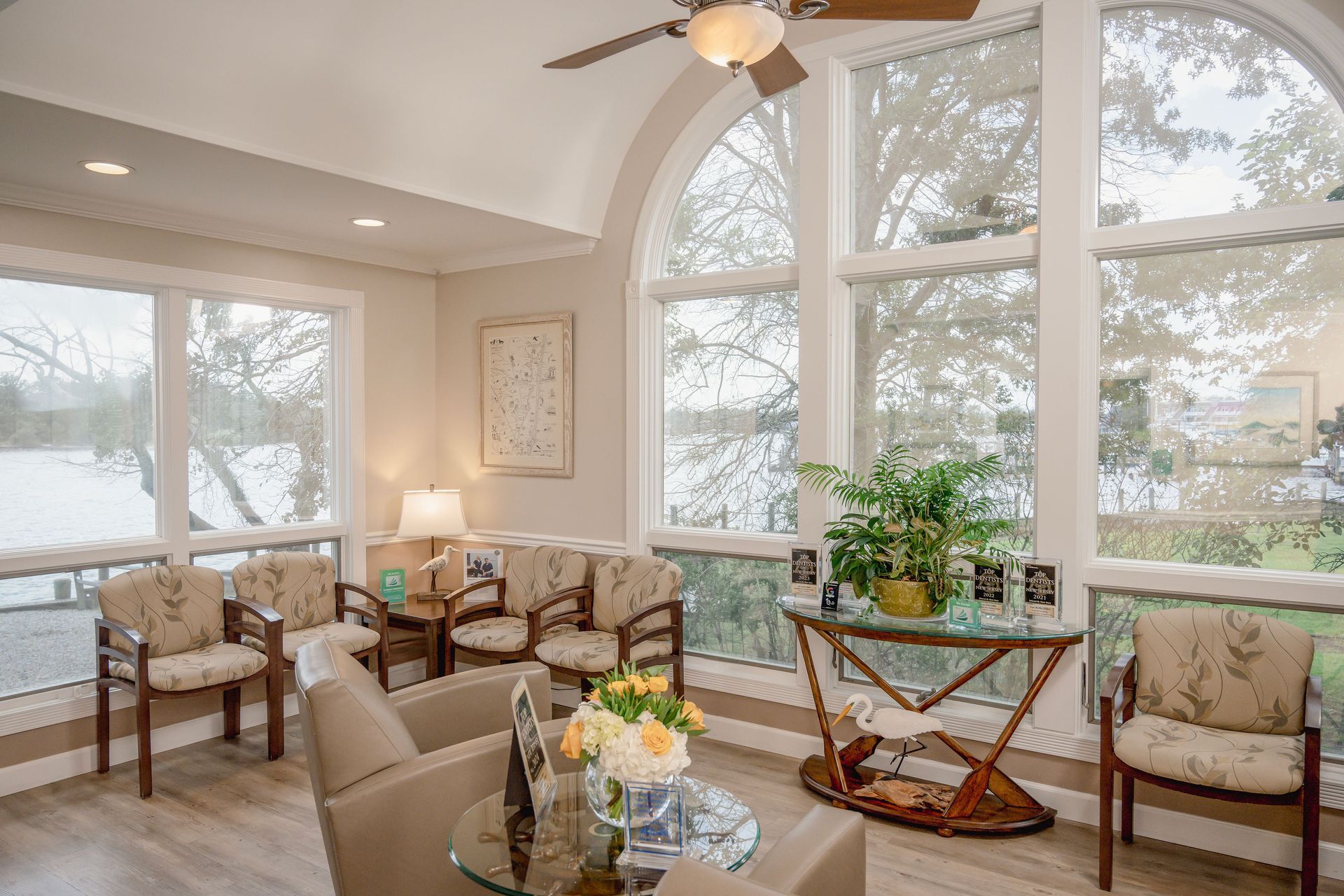 Sunroom with multiple armchairs, side table with plants, large windows overlooking outdoor view.