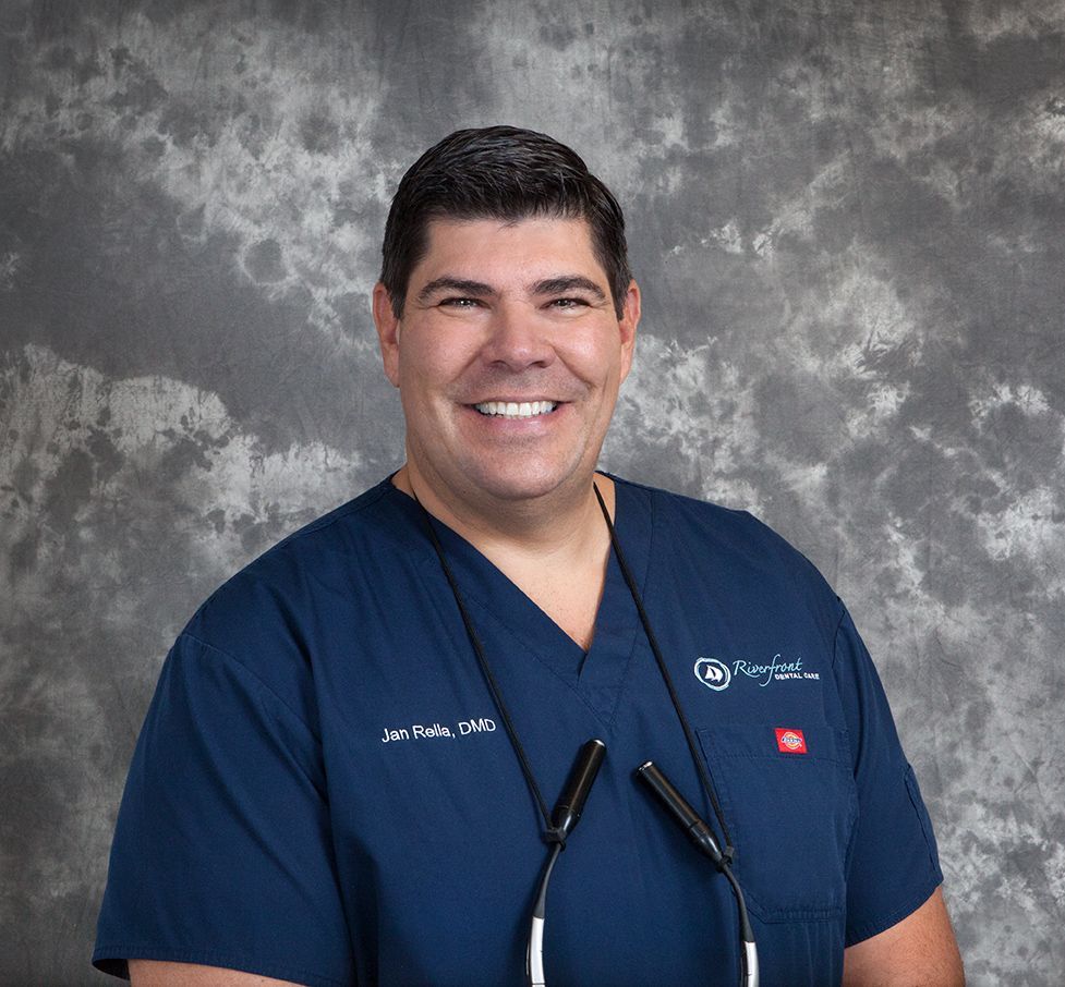 Smiling man in blue scrubs, stethoscope, gray background.