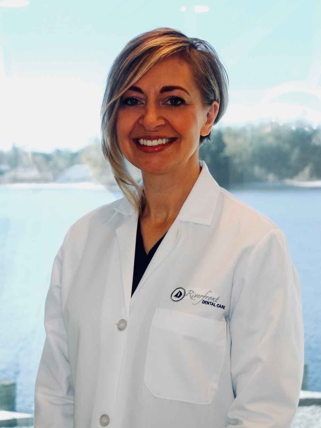 Woman in white coat, smiling, near a window.