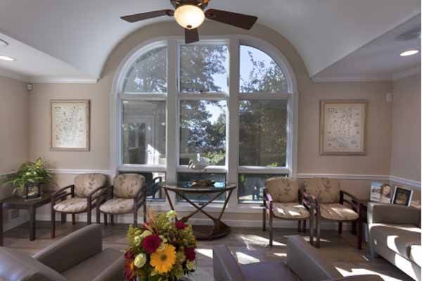 Waiting room with chairs, large window, ceiling fan, and flower arrangement.