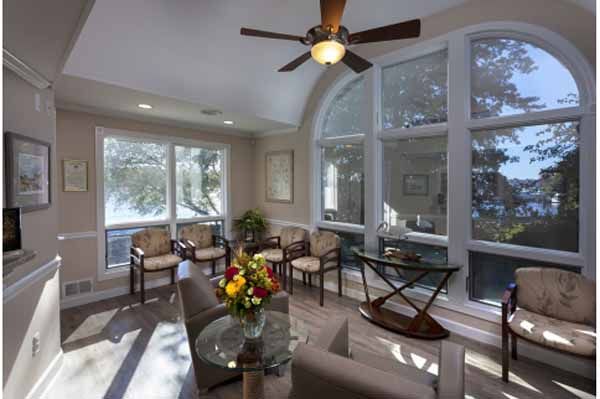 Bright room with large windows, several chairs, a table, and a ceiling fan.