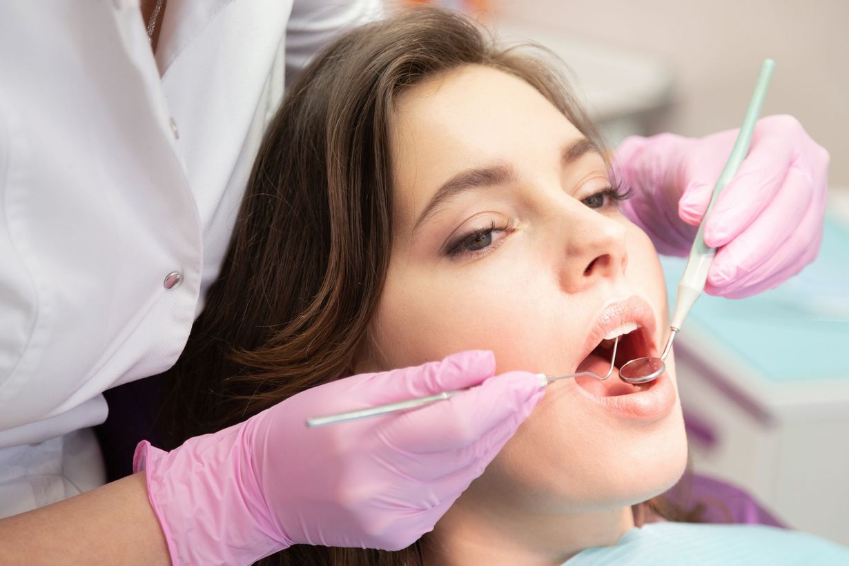 Dentist examining a patient's open mouth with gloved hands and dental tools