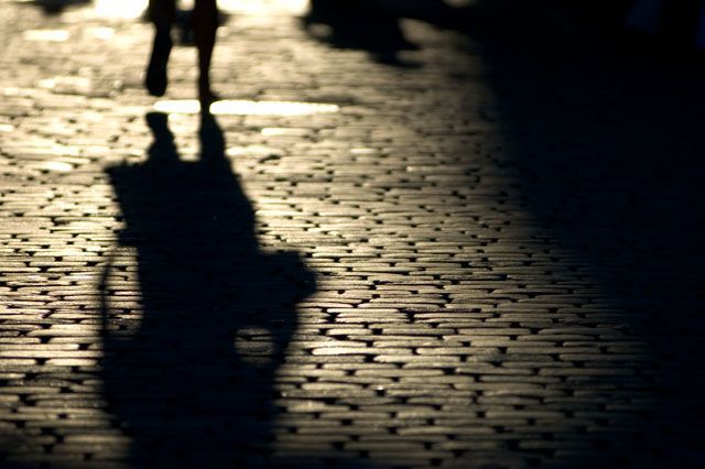 Shadow of a person walking on cobblestone street, lit by sunlight.