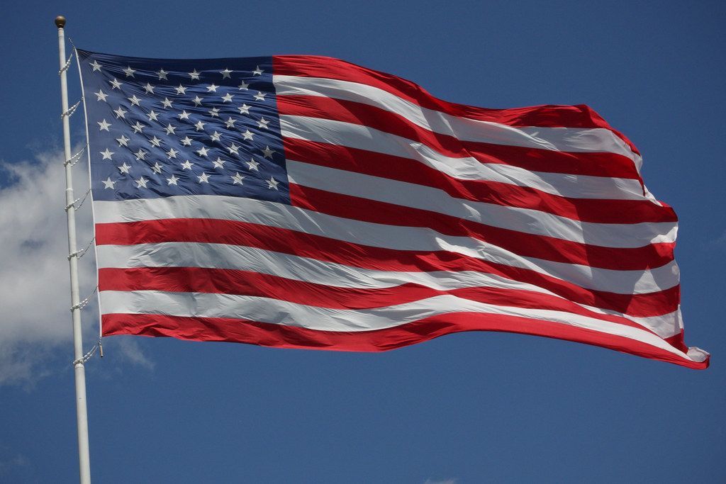 American flag waving in the wind against a blue sky with some clouds.