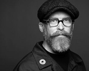Man with glasses, a beard, and a hat, looking at the camera.