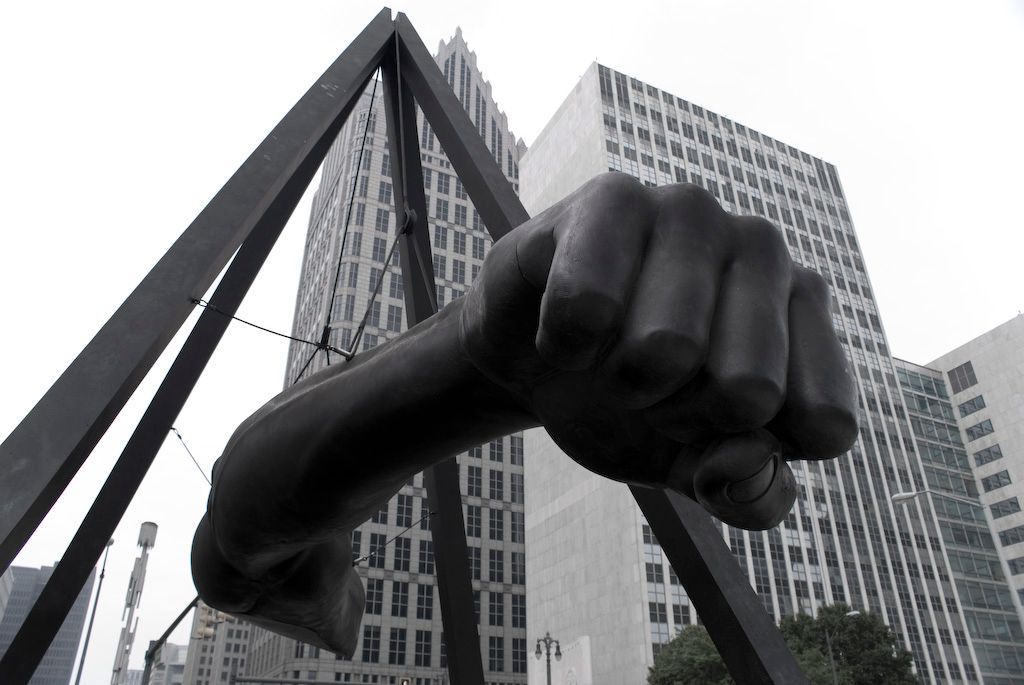 Black clenched fist sculpture with city buildings in background.