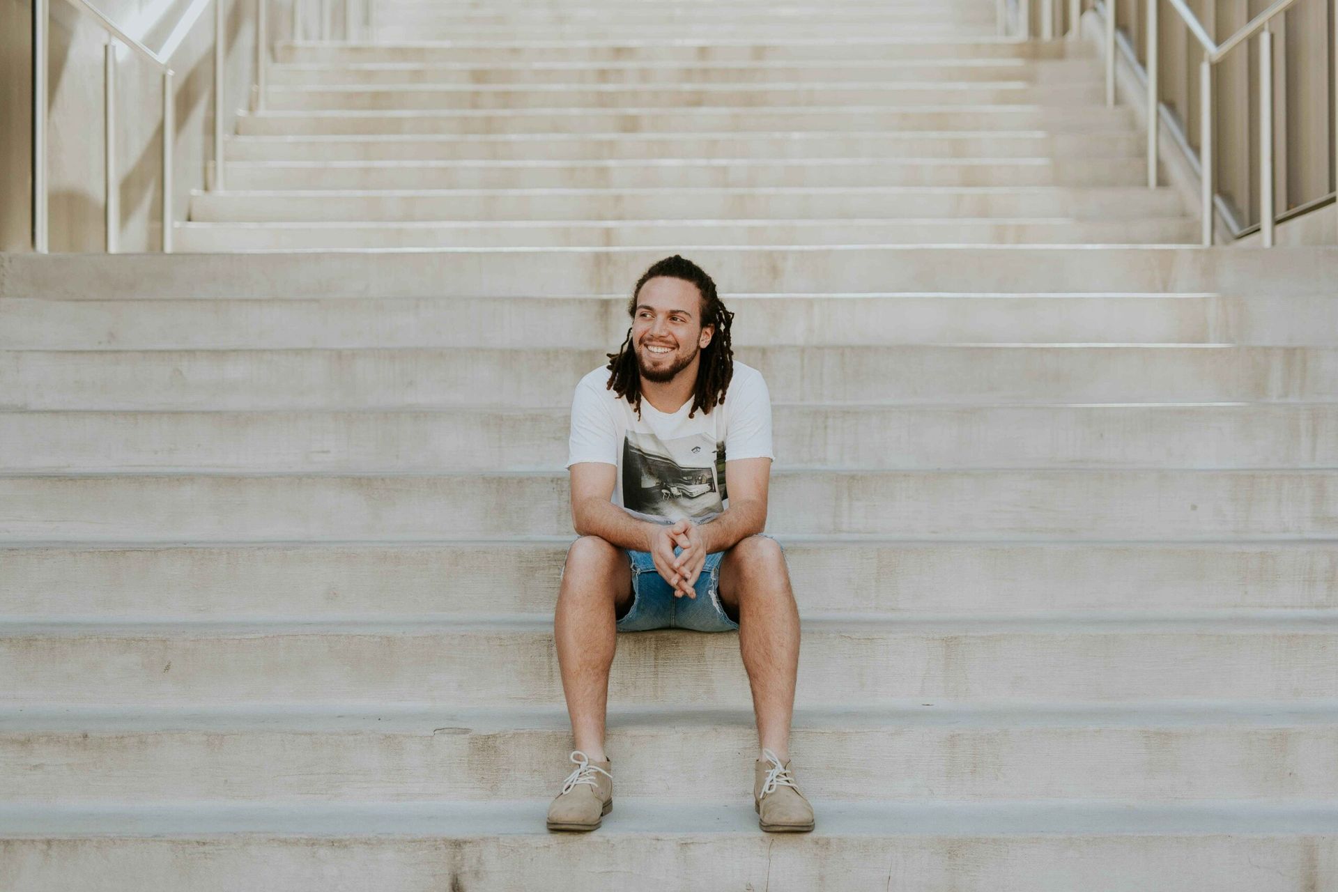 Man with long hair sits smiling on concrete steps.