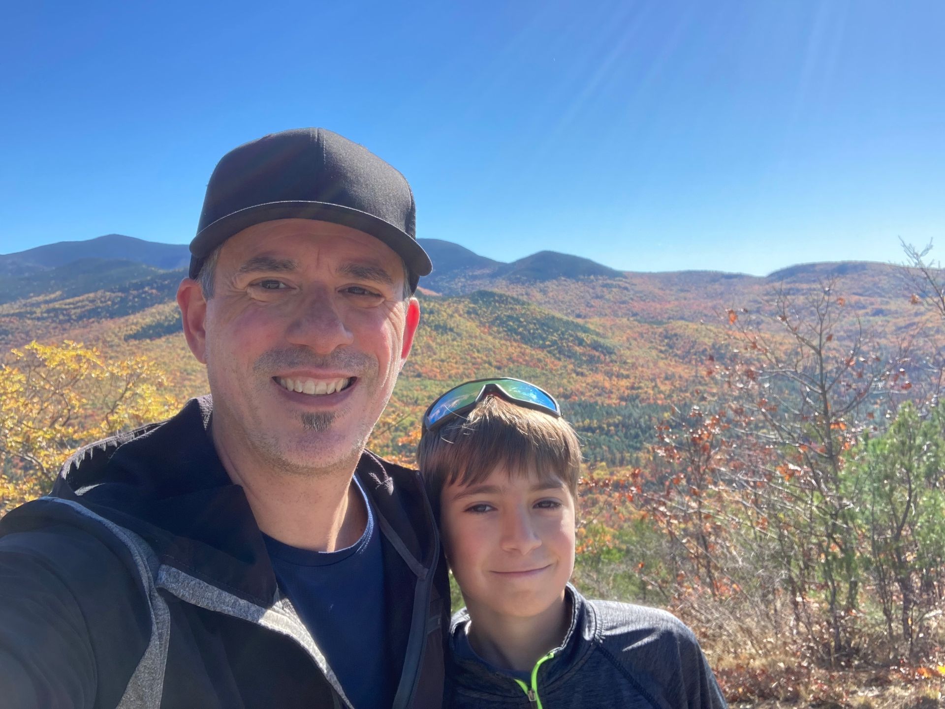 Two people smiling with a mountain vista and autumn foliage in the background