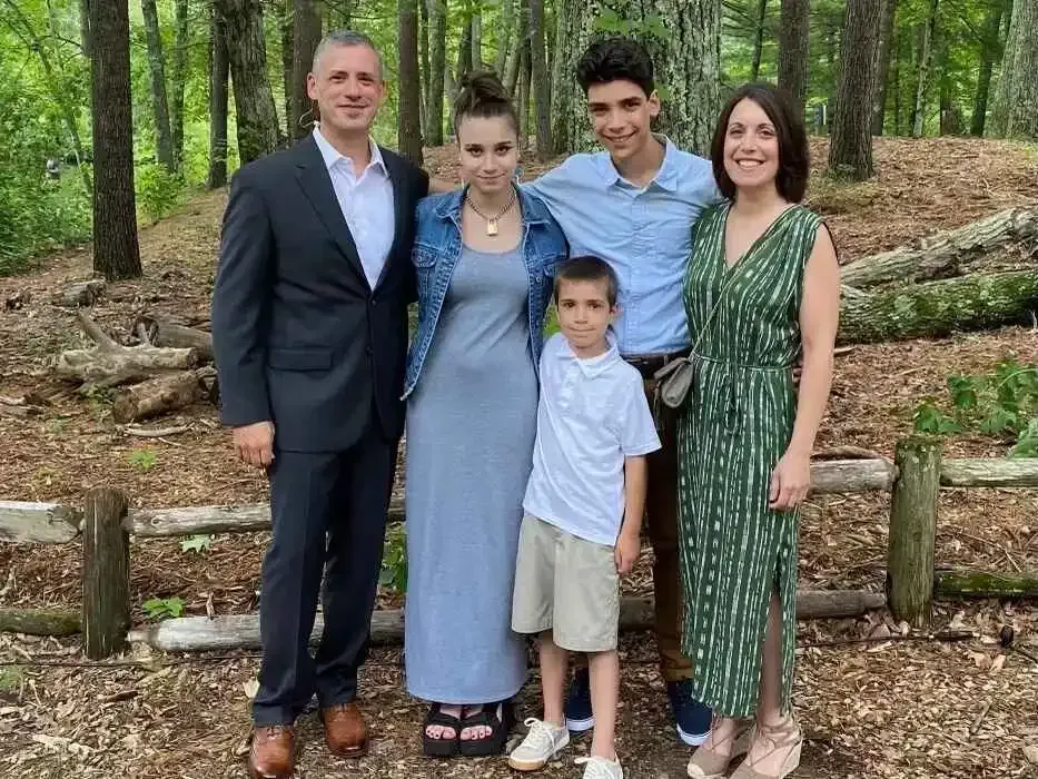 Family of five standing together in a wooded park, dressed semi-formally, smiling at the camera.