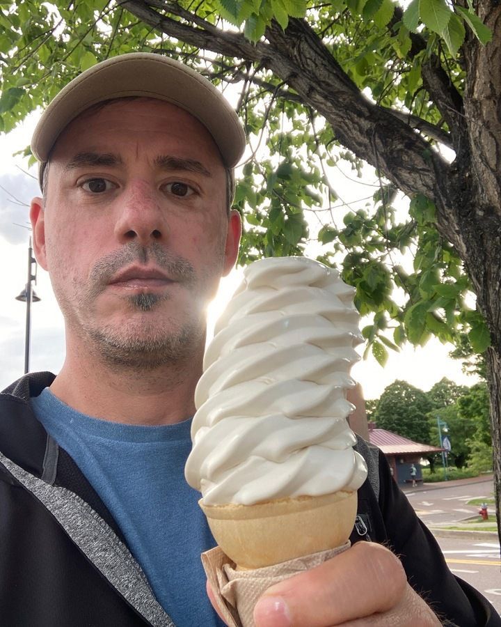 Man holding a large swirl soft serve ice cream cone, outdoor setting.