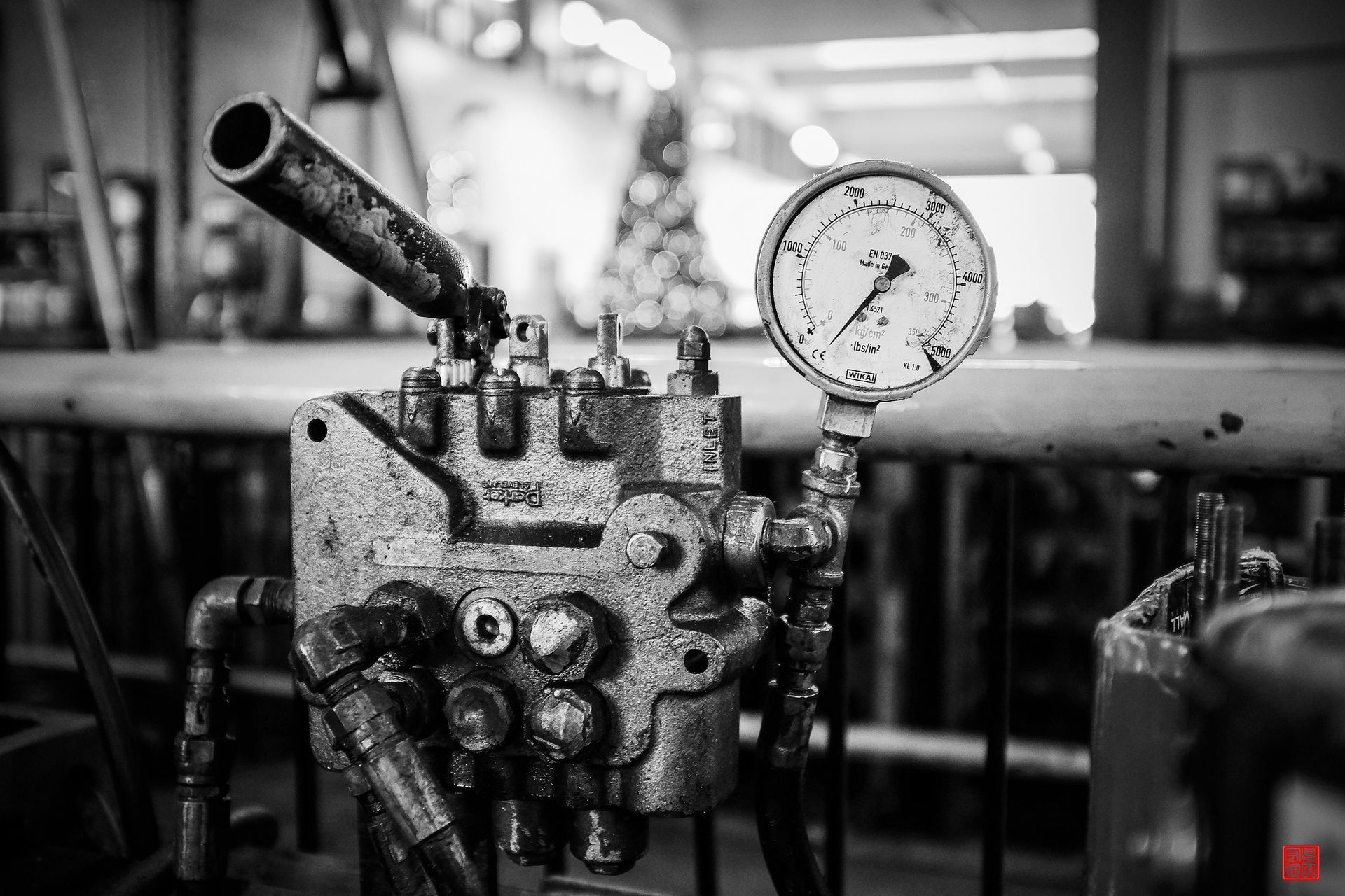 Black and white photo of old industrial machinery, featuring a pressure gauge and pipes in a factory setting.
