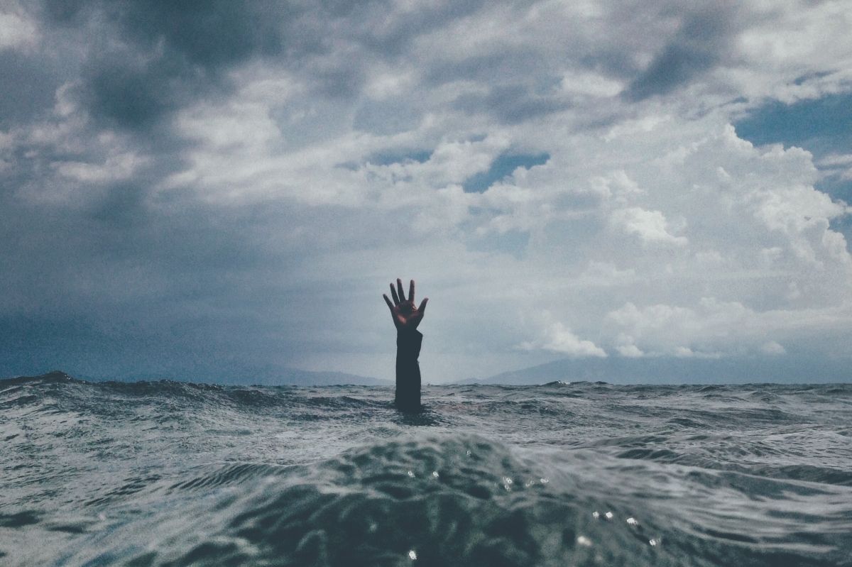 Hand reaching out of stormy ocean under a cloudy sky.