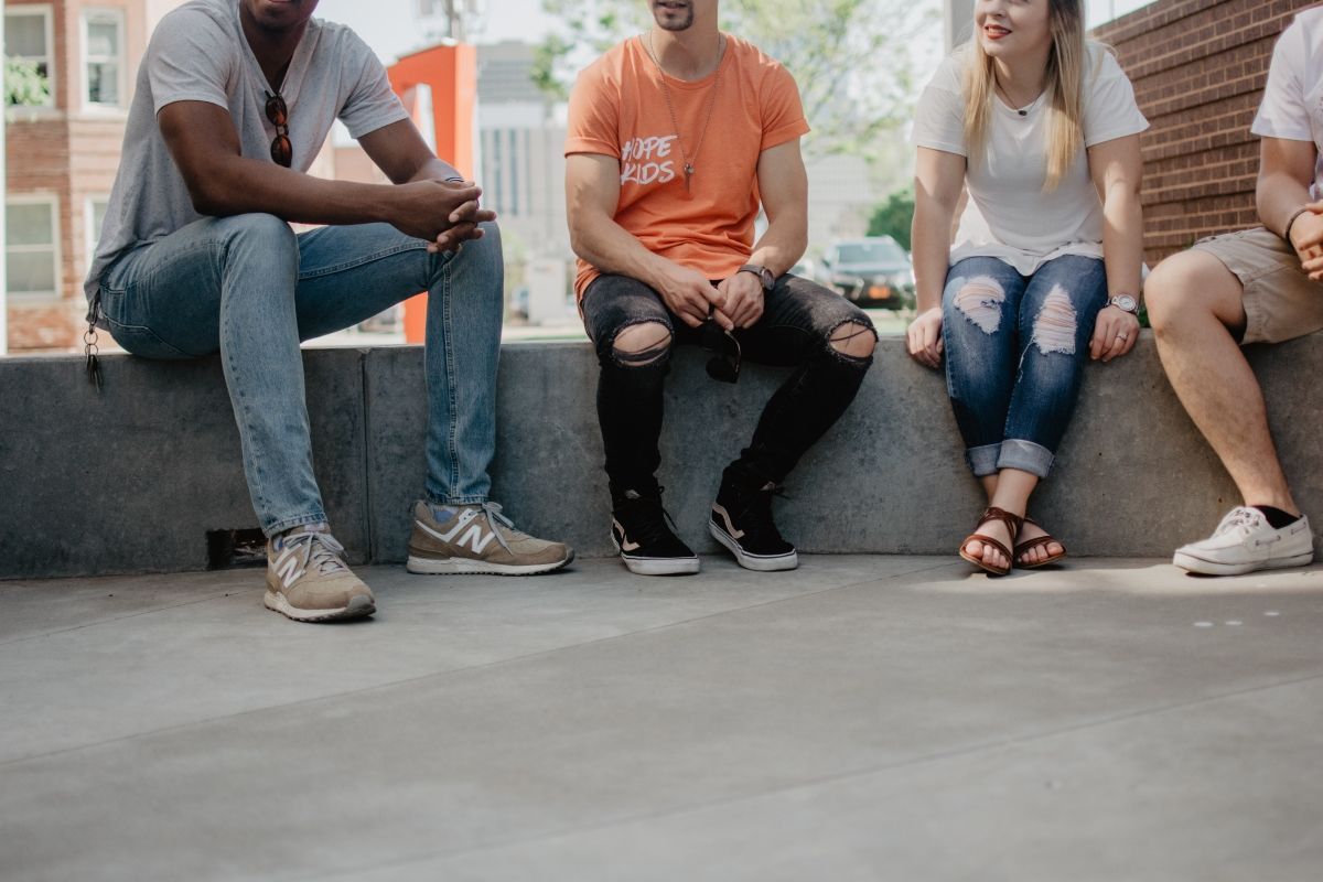 Four young people sitting on a concrete ledge, smiling. Sunny day.