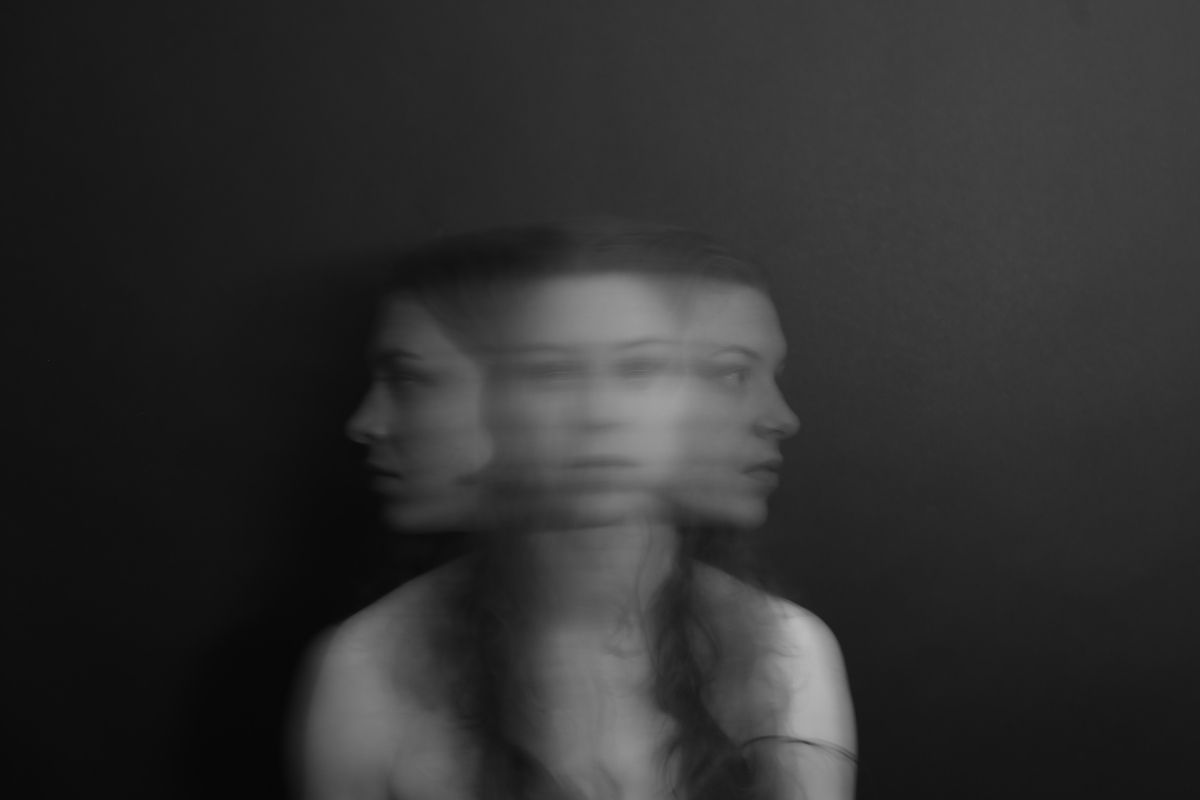 Blurred, black and white portrait of a woman with multiple faces, against a dark background.