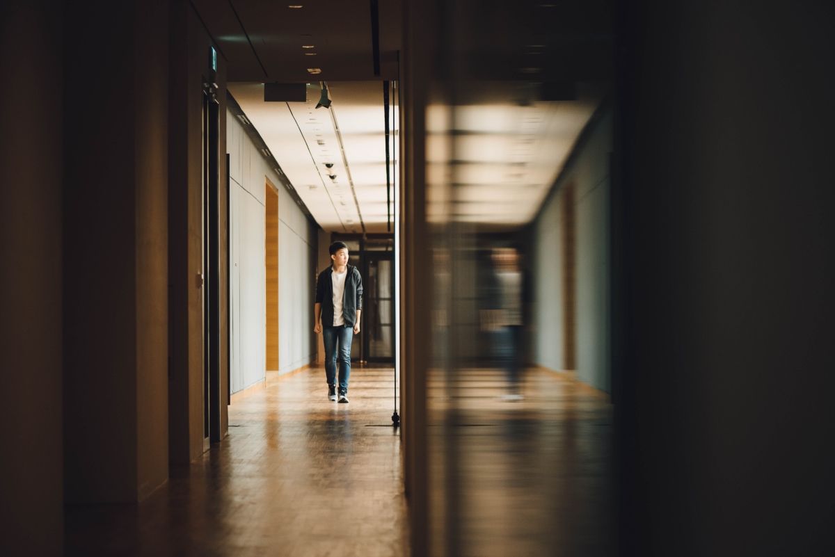 Person walking down a long, well-lit hallway. Reflection in glass.
