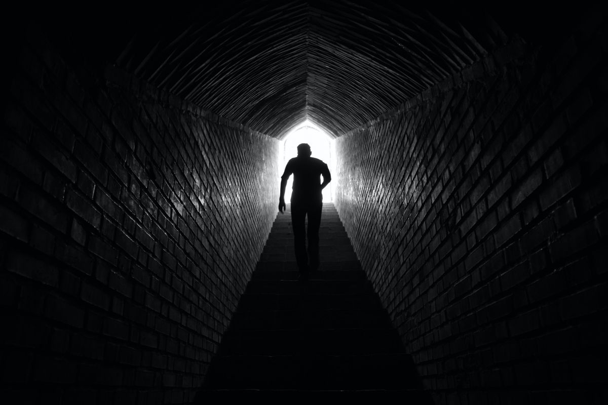 Silhouette of a person walking toward bright light at the end of a dark tunnel.