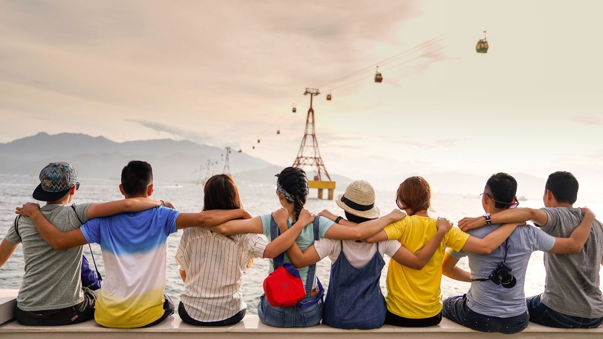 Friends with arms around each other, overlooking a coastal view with cable cars.
