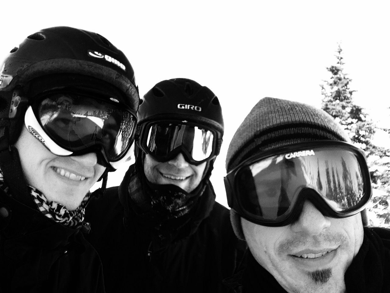 Three people in ski goggles and winter hats smiling outdoors in snowy conditions