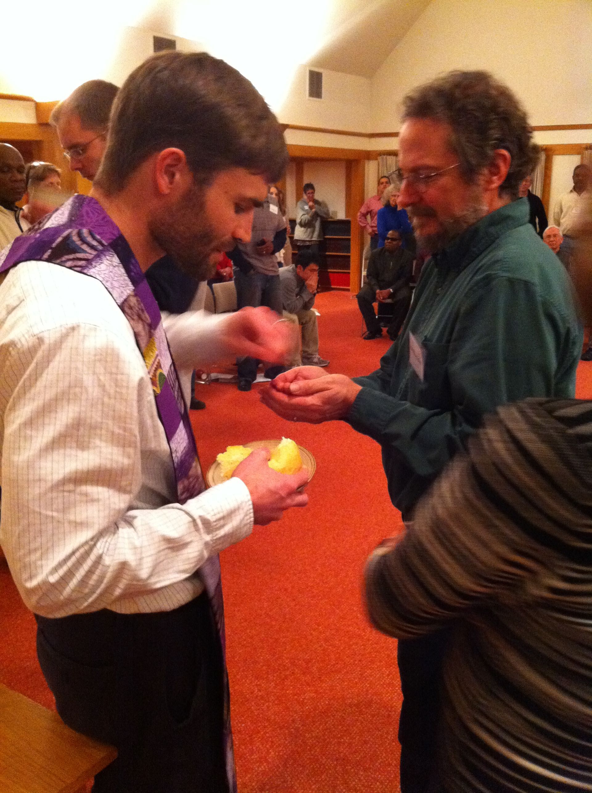 Man in clergy garb offering something to a man's open hands during a religious service.