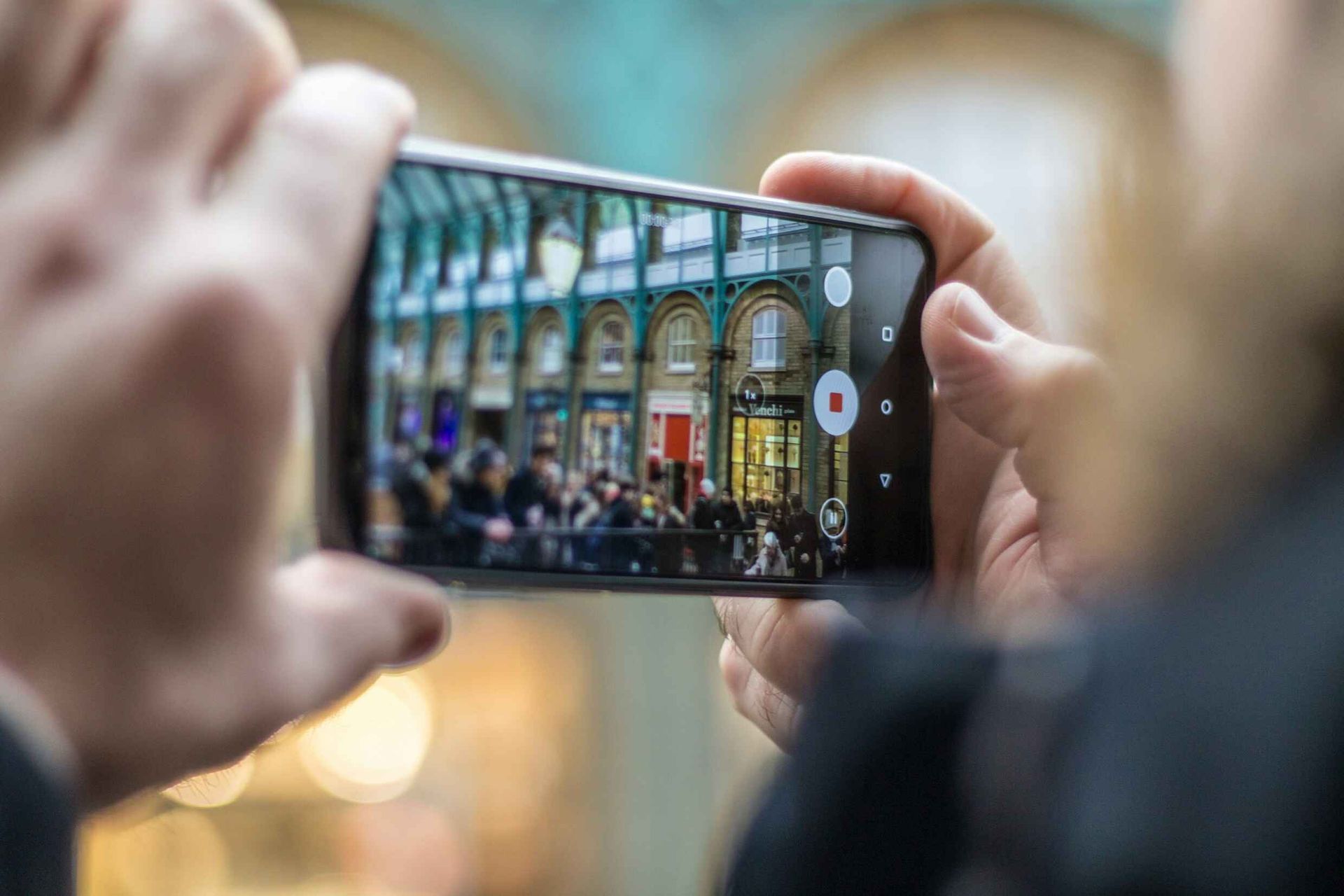 Person taking photo of a building interior with shops, using a smartphone.