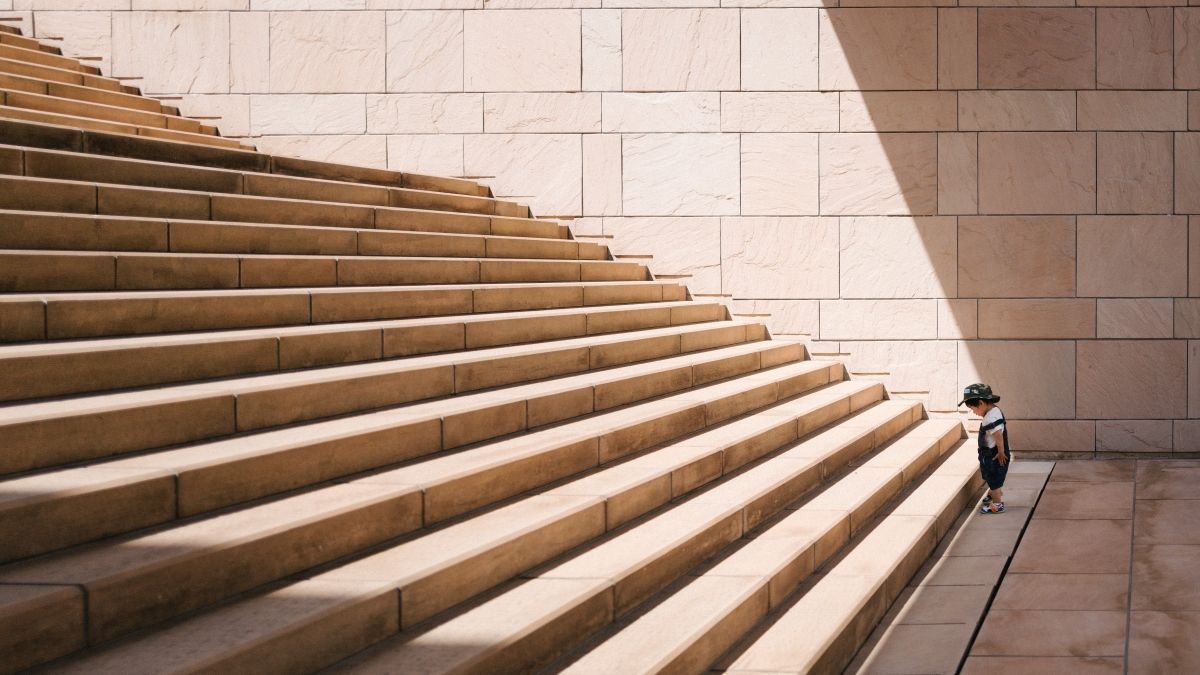 Child standing at the bottom of long, stone staircase, bathed in sunlight.