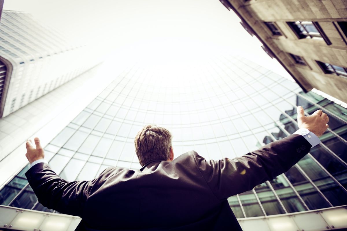 Man with arms outstretched stands before a tall building, celebrating success.