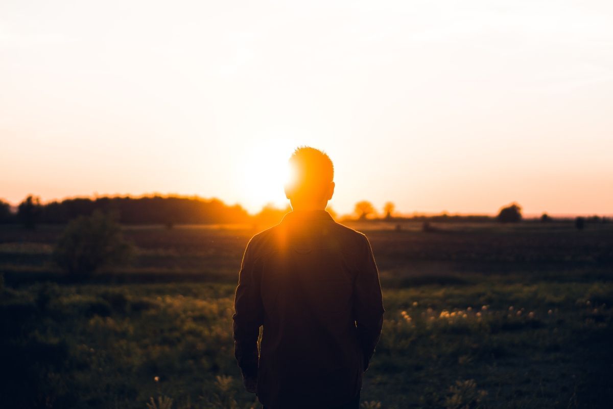 Person silhouetted against a sunset in a field; warm orange and yellow hues.