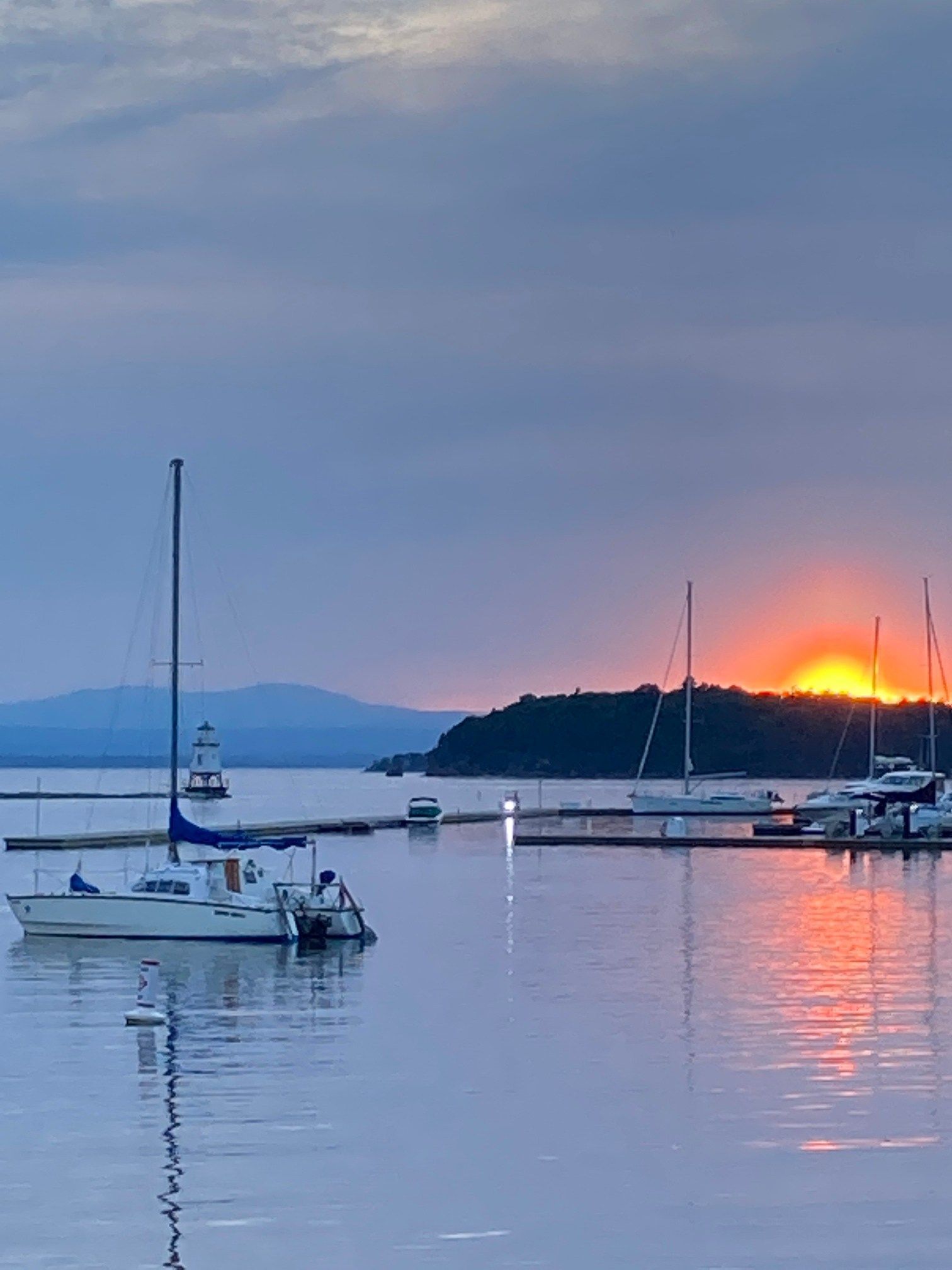 Boats in a harbor reflect the sunset. Silhouettes of boats and land under a colorful sky.