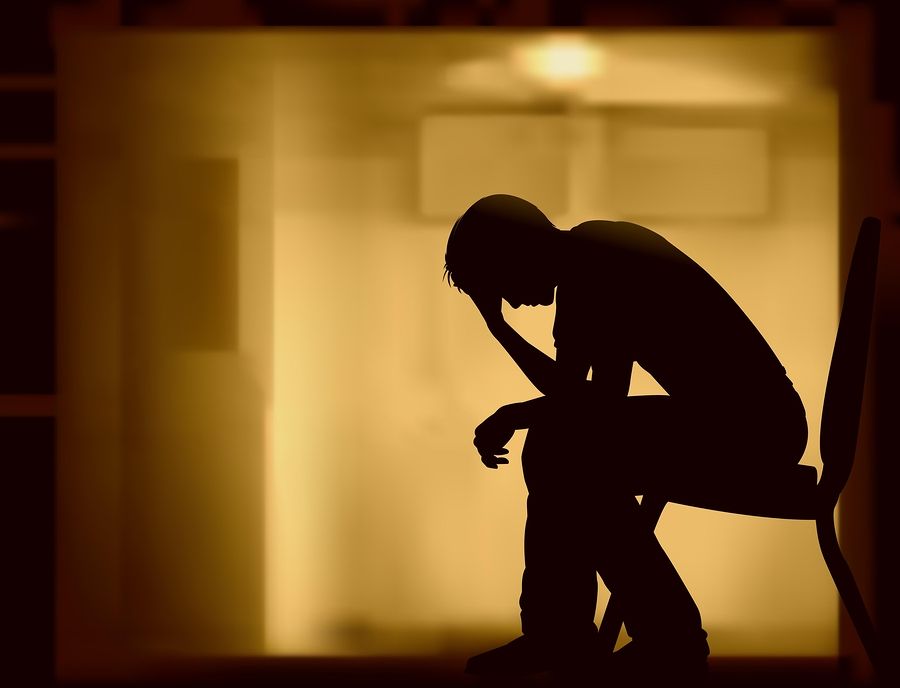 Silhouette of a person sitting with head in hand, appearing sad, in a dimly lit hallway.