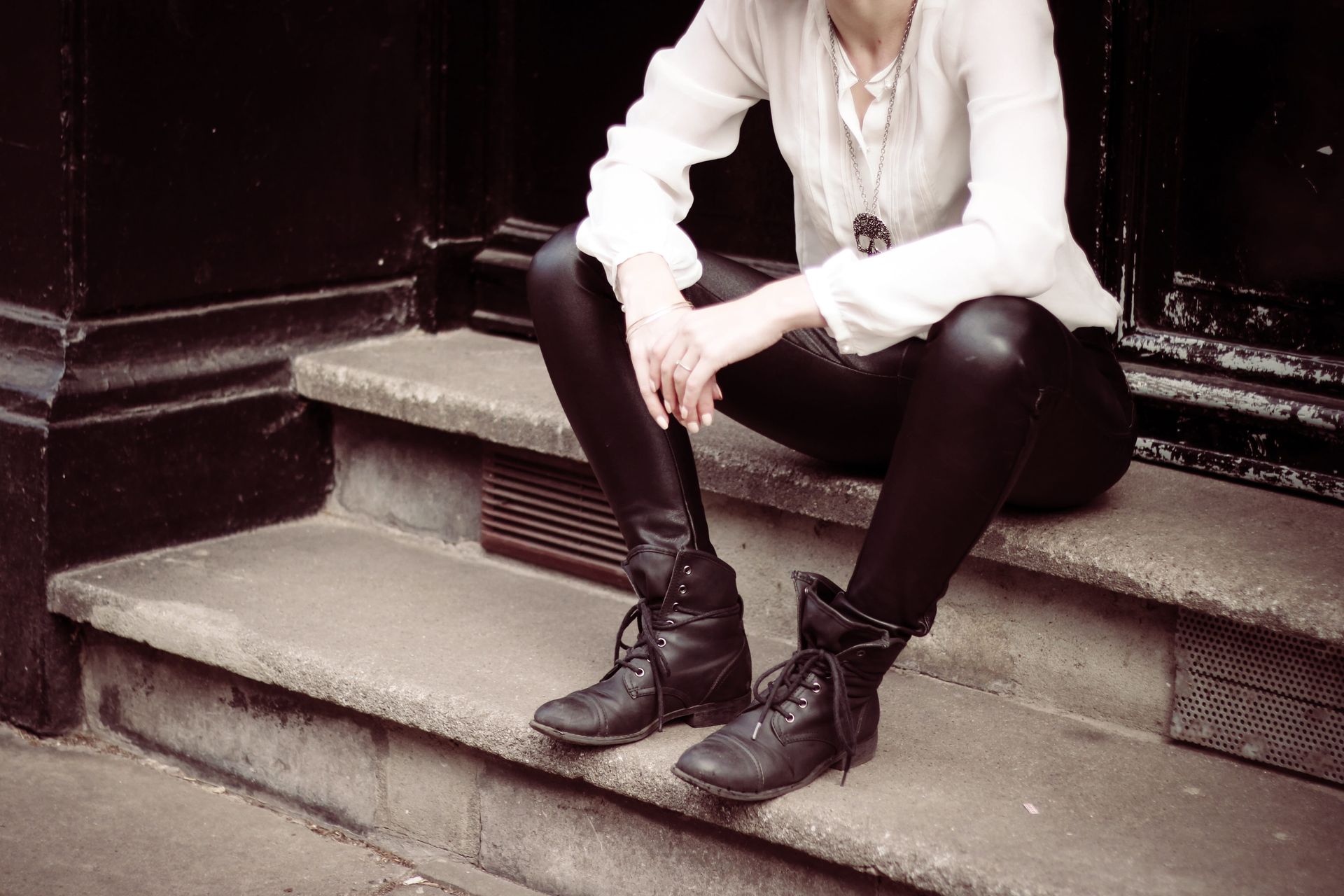 Woman sitting on steps, wearing black leather pants, boots, and a white blouse.