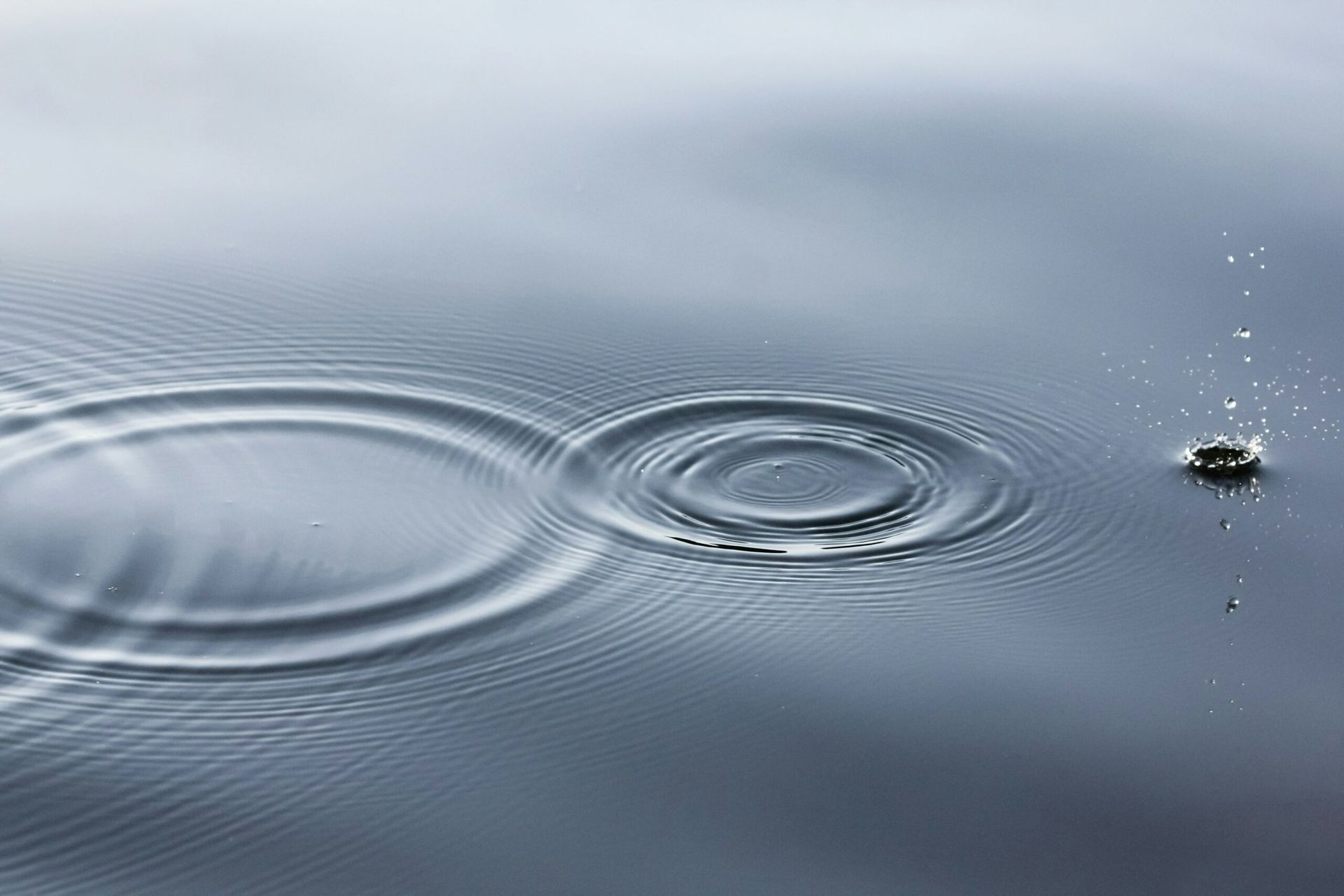 Concentric ripples on water's surface expand outward from a point, with a splash nearby.