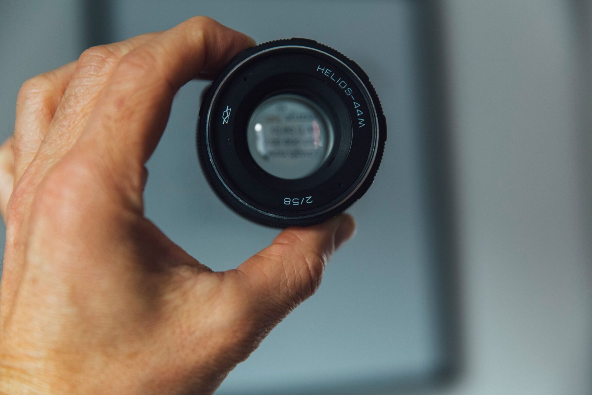 Hand holding a camera lens, with a blurred background.