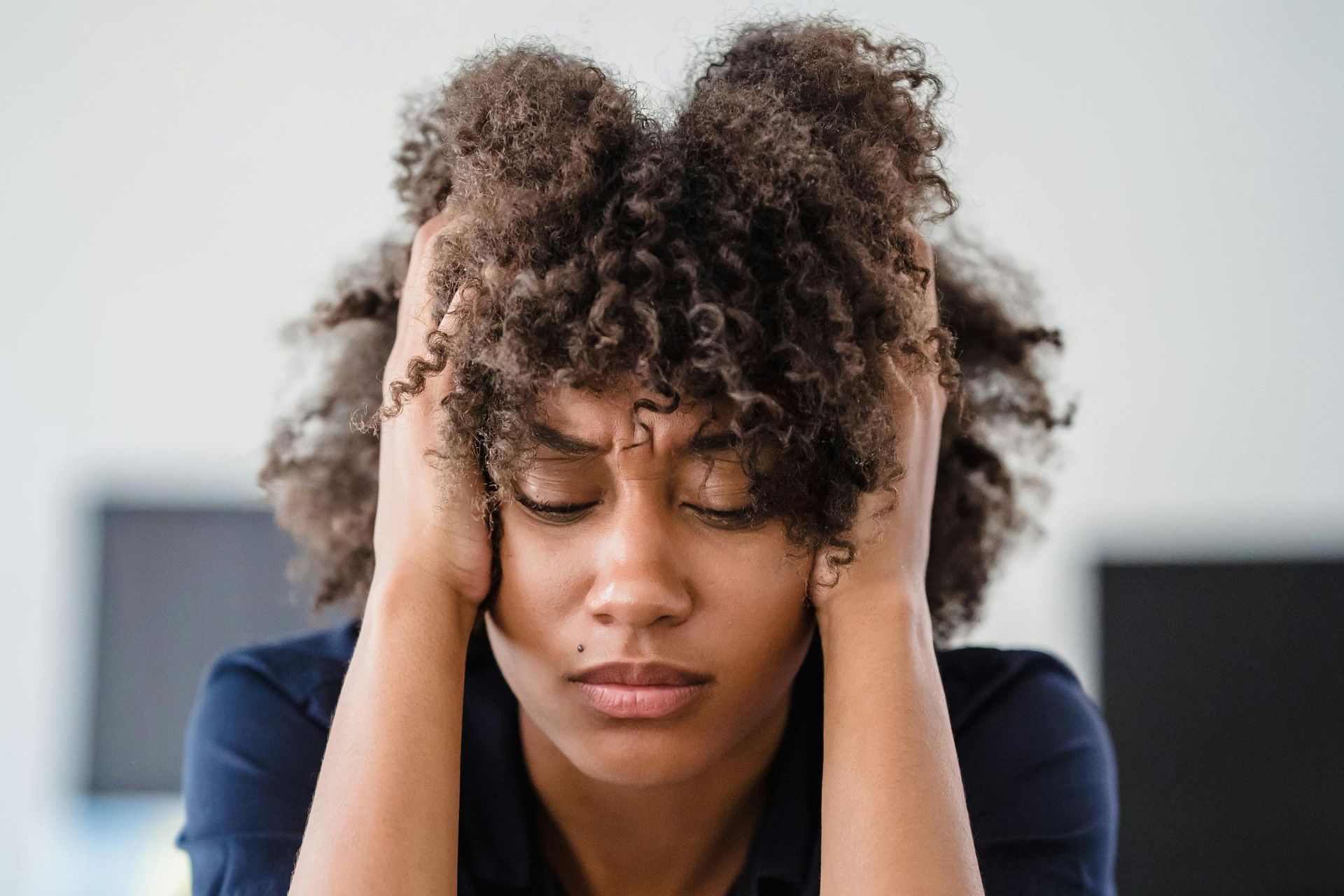 Woman with curly hair holding her head and looking stressed indoors
