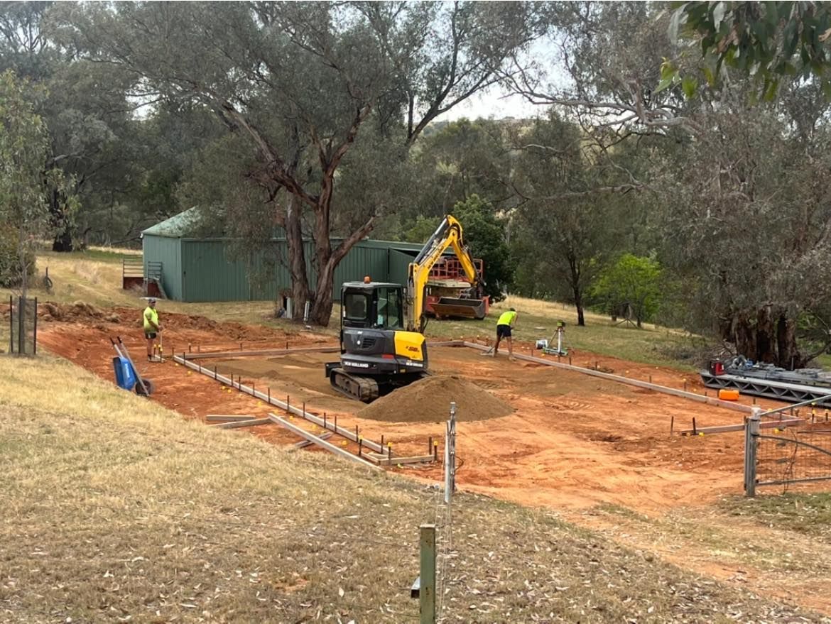 A yellow excavator is working on a dirt road in a field.