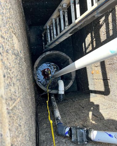 An overhead view of a concrete pit containing a sump pump with a white discharge pipe, a yellow cord, and a metal ladder.