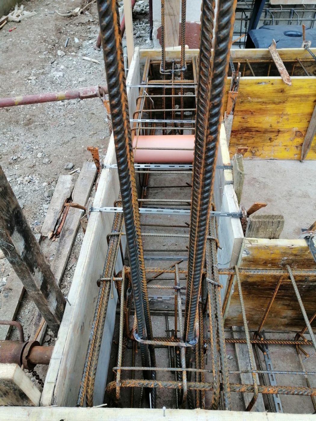 Gabbia di barre d'acciaio installata all'interno di casseforme in legno per una fondazione in calcestruzzo, con tubo di drenaggio arancione integrato.