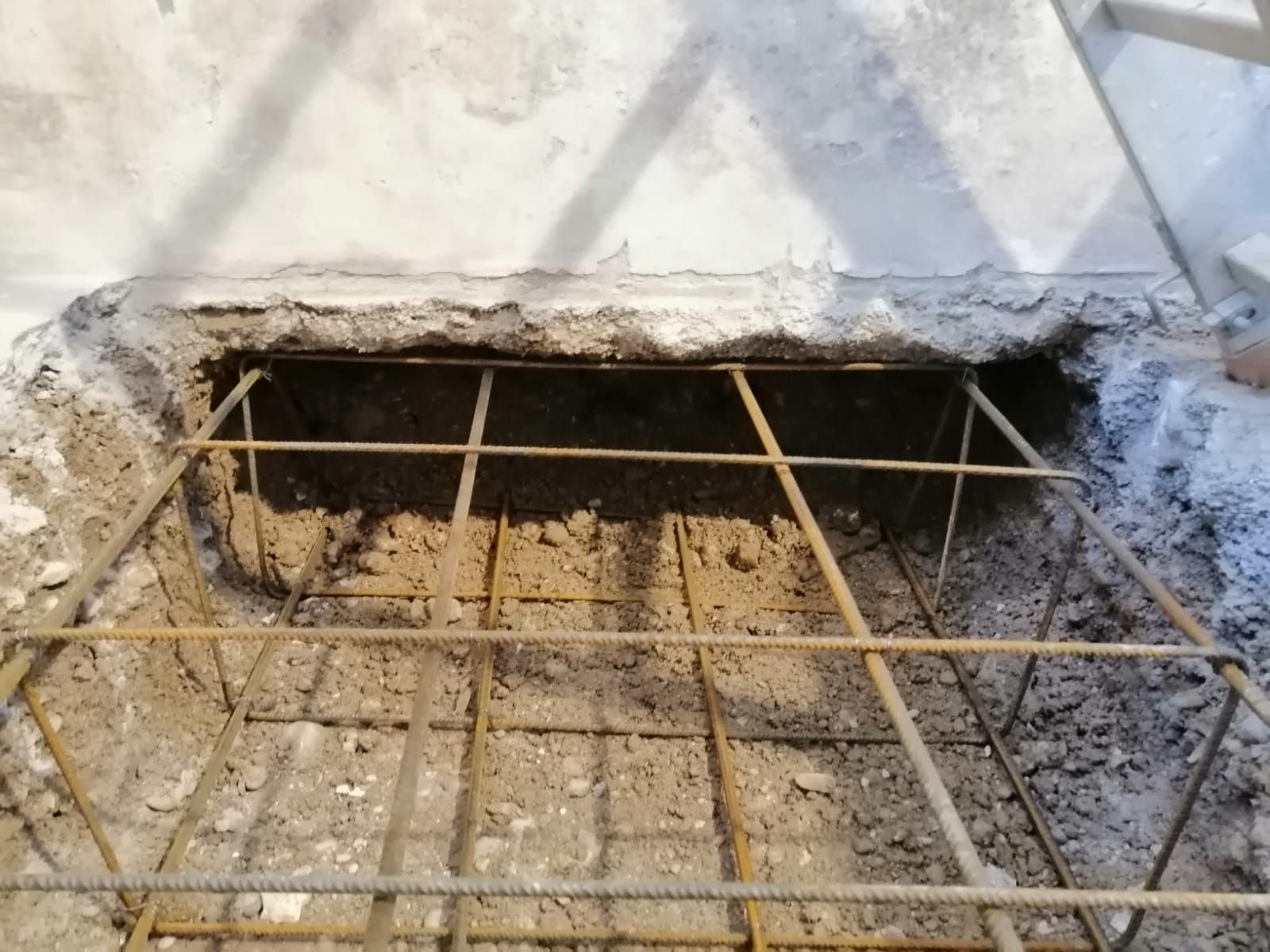 Durante i lavori di costruzione, all'interno di uno scavo nel terreno, vicino a un muro di cemento, si trova una gabbia quadrata di barre d'armatura metalliche.